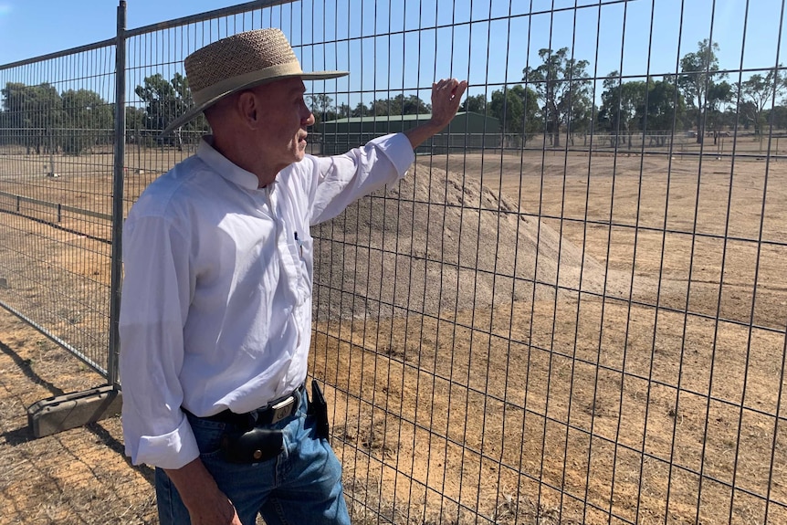 Man in hat leans against wire fence