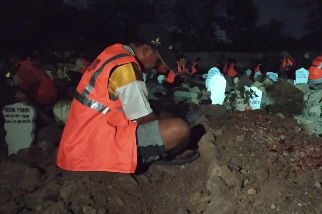 A man sitting next to a grave at night time with his head looking down