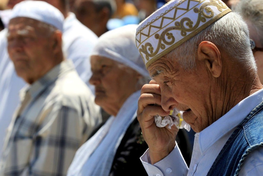 An elderly man wipes away a tear in traditional dress