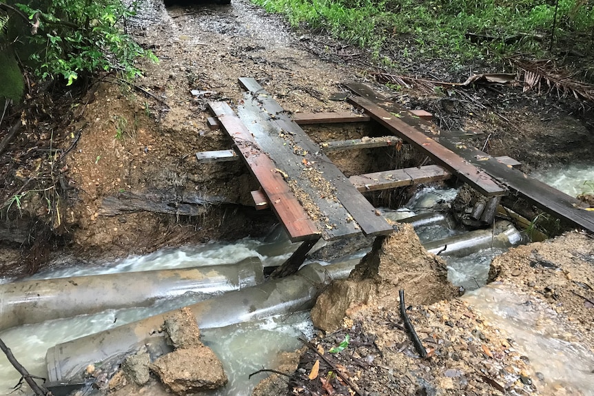 A damaged timber bridge, with a road washed out.