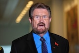 Justice Party senator Derryn Hinch wears a red ribbon as he speaks to reporters regarding 18c in Parliament House