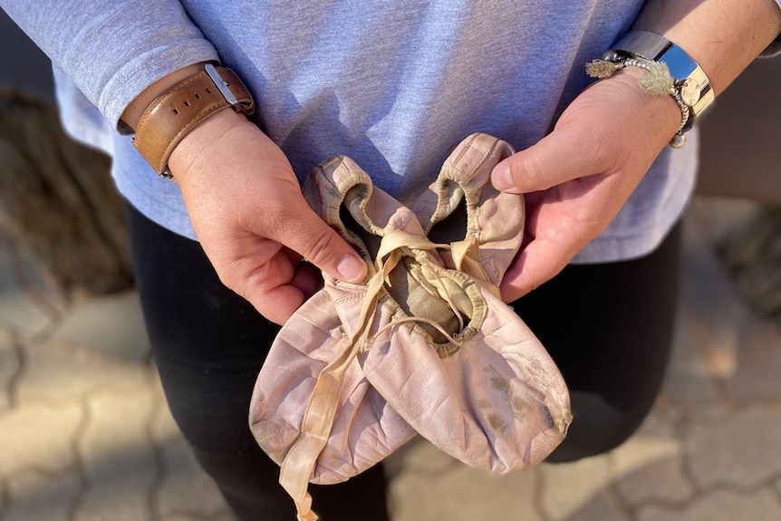 Woman holding pair of ballet flats from her childhood 