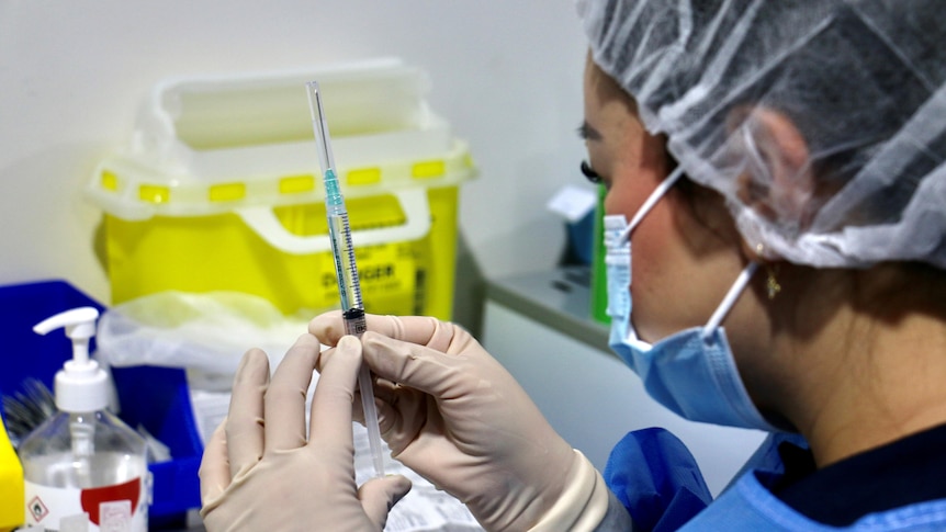 A close-up shot of a woman wearing PPE handling a syringe filled with the Pfizer COVID-19 vaccine.