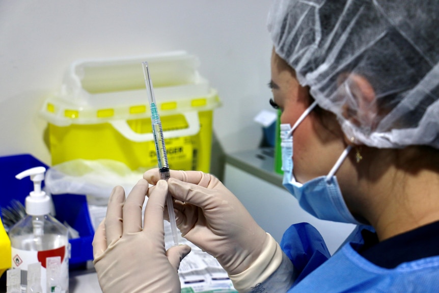 A close-up shot of a woman wearing PPE handling a syringe filled with the Pfizer COVID-19 vaccine.