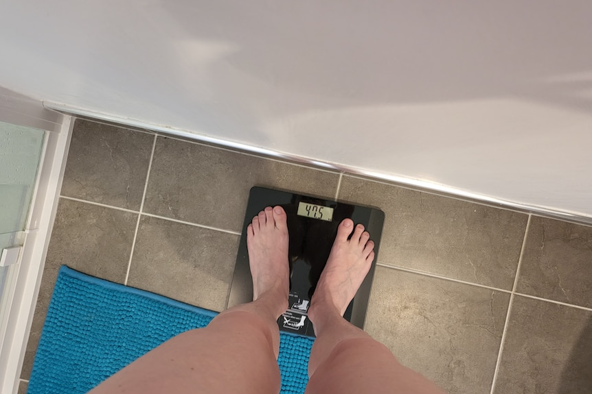 A woman's legs stand on a set of bathroom scales. 
