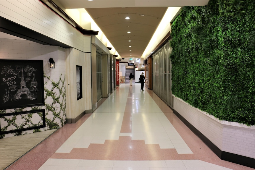 A near-deserted shopping mall with a woman in the background walking towards the camera.