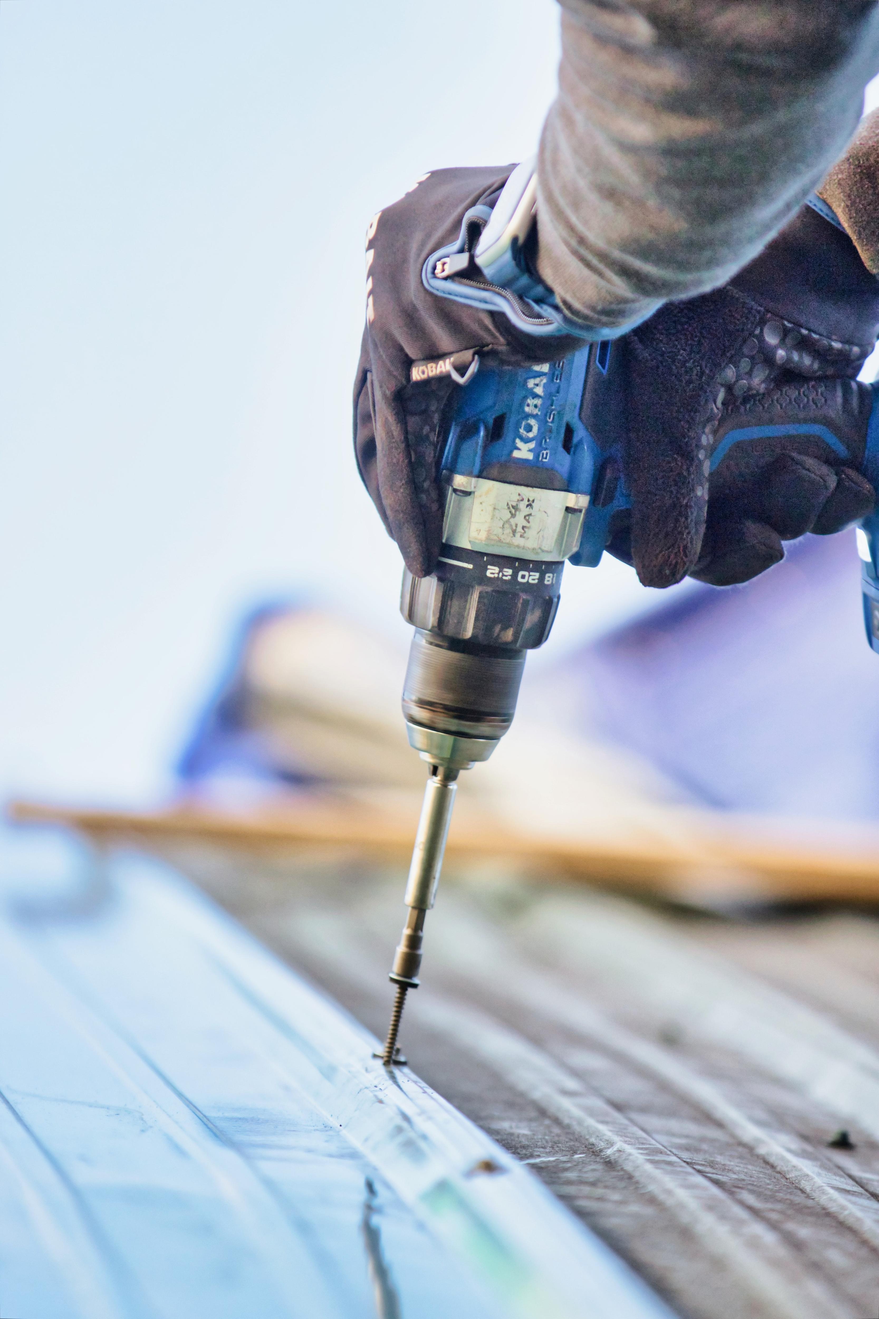 A man uses a drill to fix a roof.