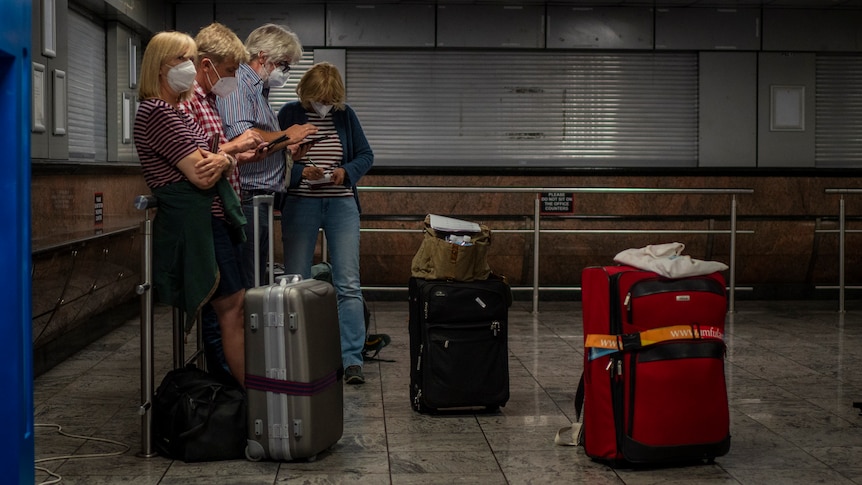Una famiglia è in piedi con i loro bagagli, indossando maschere per il viso, in un aeroporto vuoto.