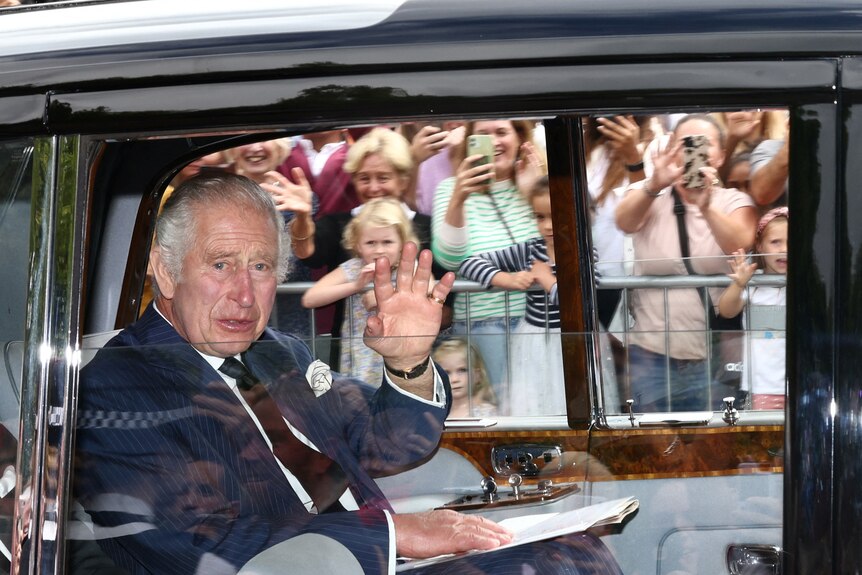 King Charles waves to the crowd from the car. 