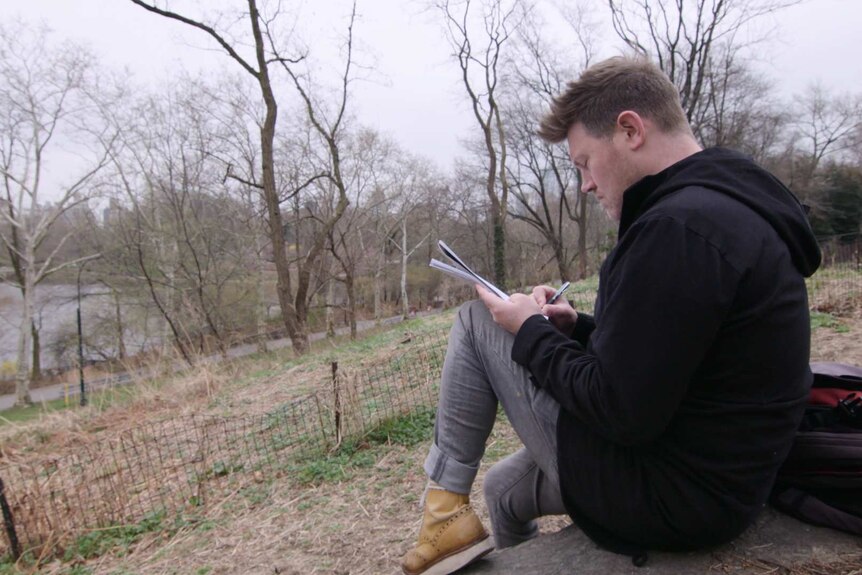 Eddie Perfect sits on a rock and writes in Central Park