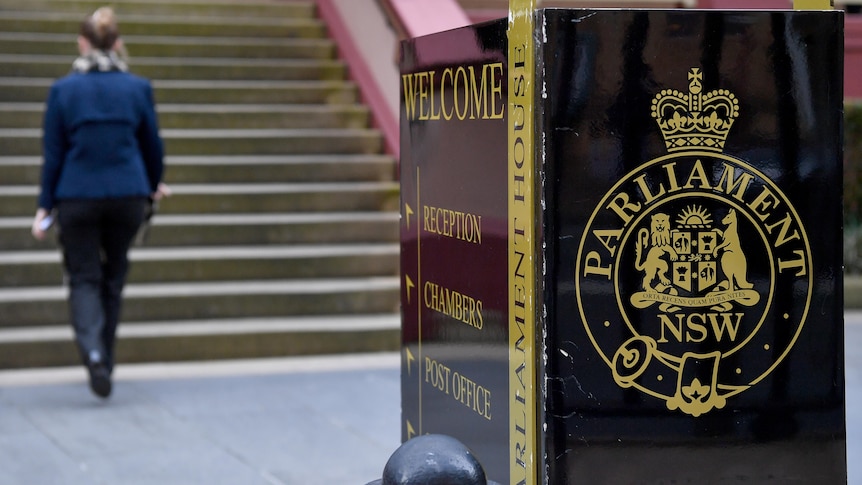 A welcome sign outside the NSW Parliament building, with a woman in the background walking up steps.