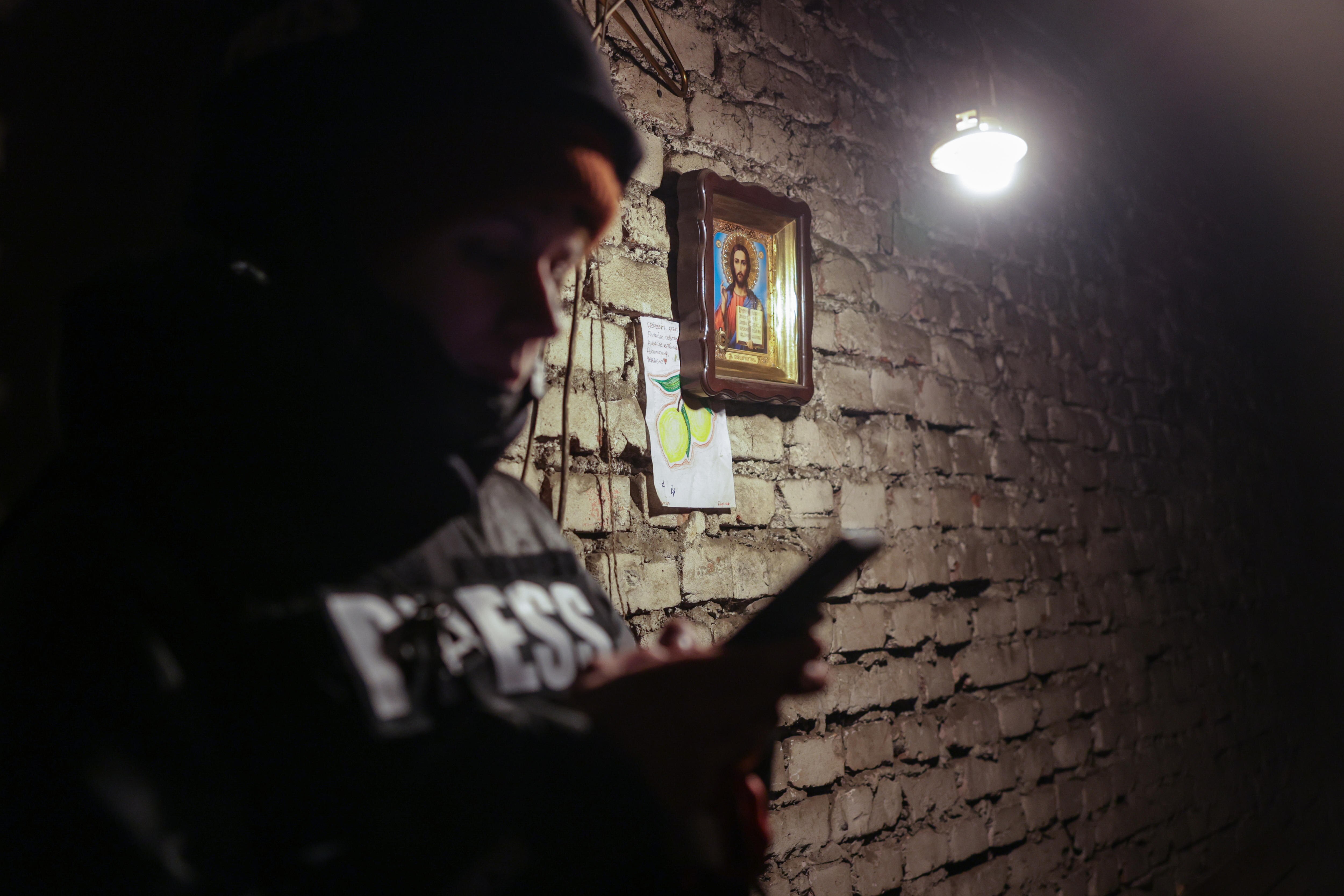 A portrait of Jesus hangs on a wall behind a woman looking on her phone.