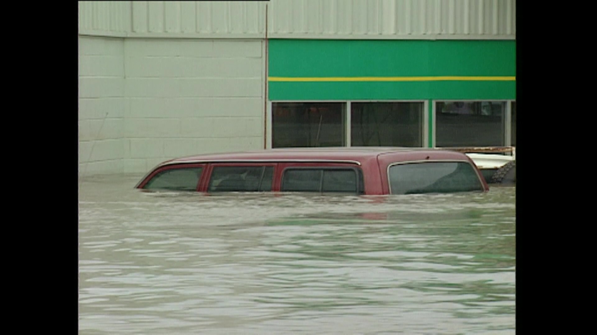 The roof of a car is visible in floodwaters, the remainder of the vehicle is underwater.