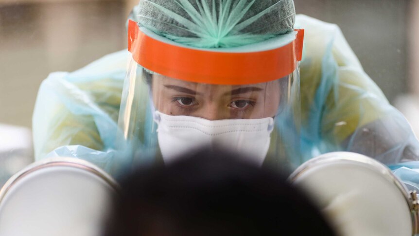 A close-up of a woman in full protective gear administering a test to a person, who we can see the back of their head.