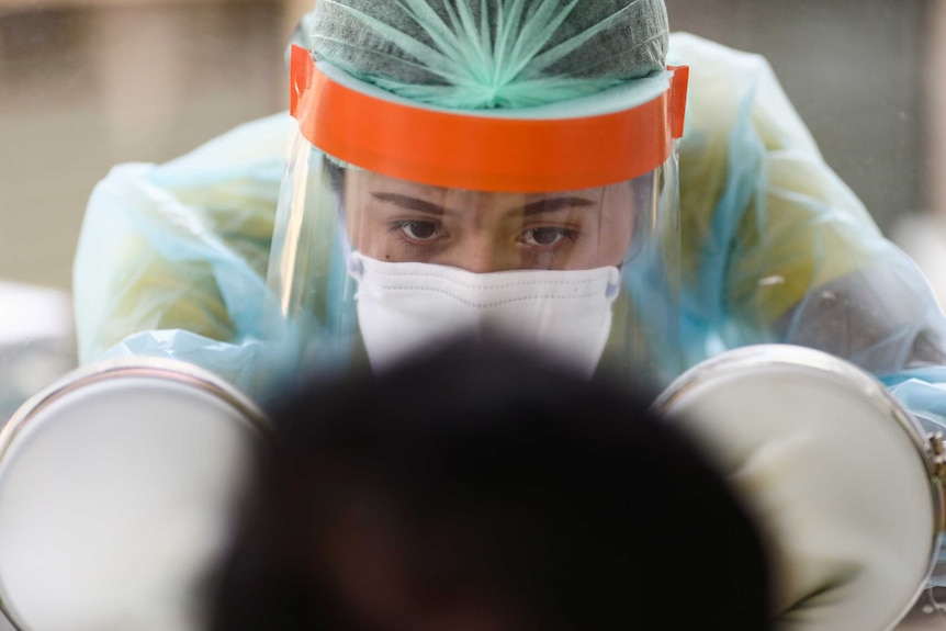 A close-up of a woman in full protective gear administering a test to a person, who we can see the back of their head.