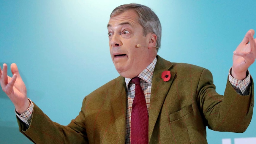 Nigel Farage wears a brown jacket, gestures with his hands in the air and a look of surprise