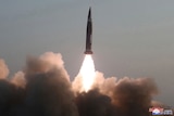 A rocket is seen firing into the air leaving a cloud of smoke below it.