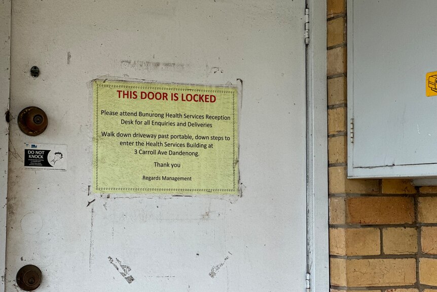 Yellow sign taped to a door on the outside of a building, saying that the door is locked.