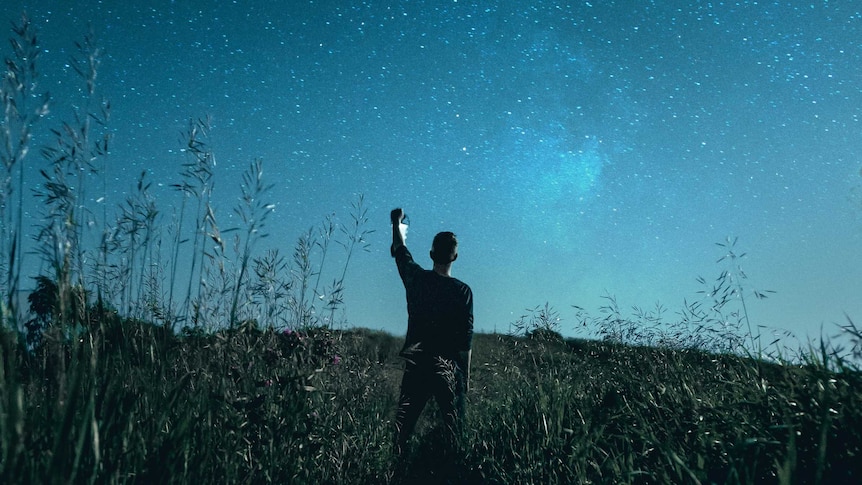 man in a field holding up his hand to the night sky