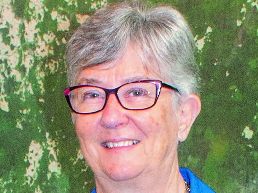 portrait of smiling Caucasian woman with cropped grey hair and rectangular-framed glasses wearing bright blue blazer