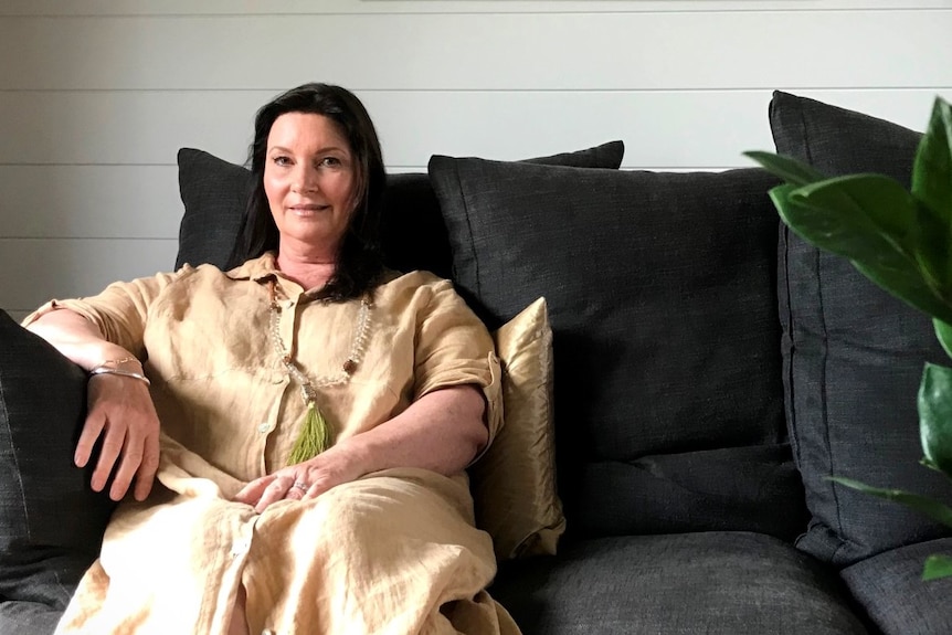 A woman in a yellow shirt dress sitting on a dark grey sofa