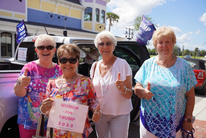 Four older women with their thumbs up holding 'women for Trump signs'