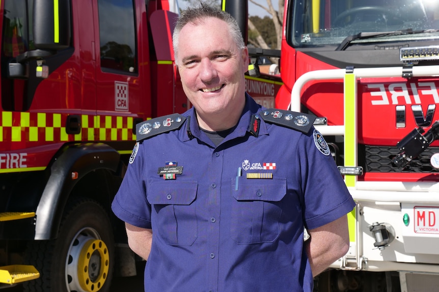 a smiling man in a blue shirt next to a fire truck