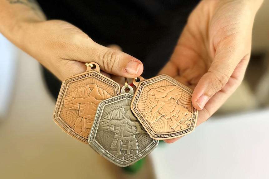 Person holds three medals at the camera