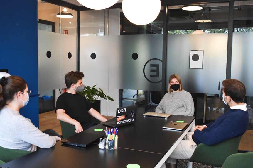 A group of people wear masks inside a meeting room at an office.