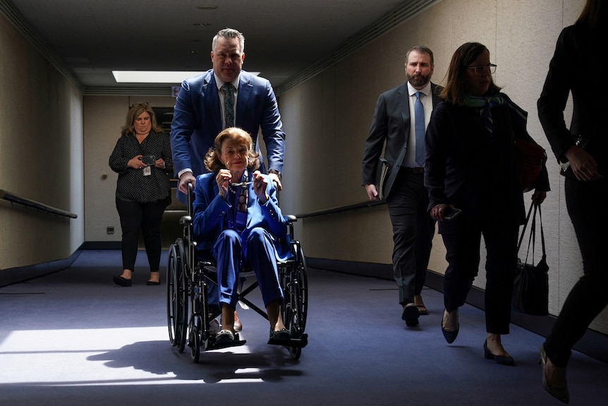 A woman wheeled in a wheelchair down a hallway 