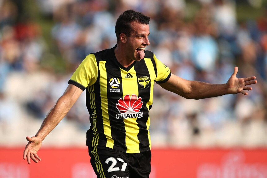 Steven Taylor holds his arms out and sticks his tongue out of his mouth whilst smiling wearing a black and yellow striped shirt