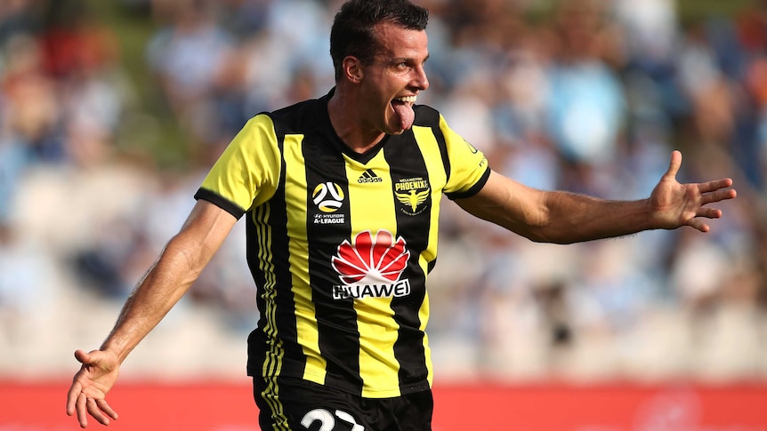 Steven Taylor holds his arms out and sticks his tongue out of his mouth whilst smiling wearing a black and yellow striped shirt