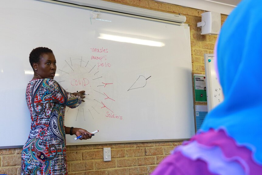A picture of Dr Barbara Nattabi standing at a whiteboard pointing to a diagram.