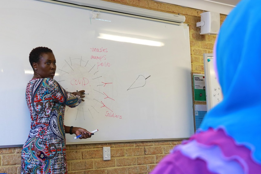 A picture of Dr Barbara Nattabi standing at a whiteboard pointing to a diagram.