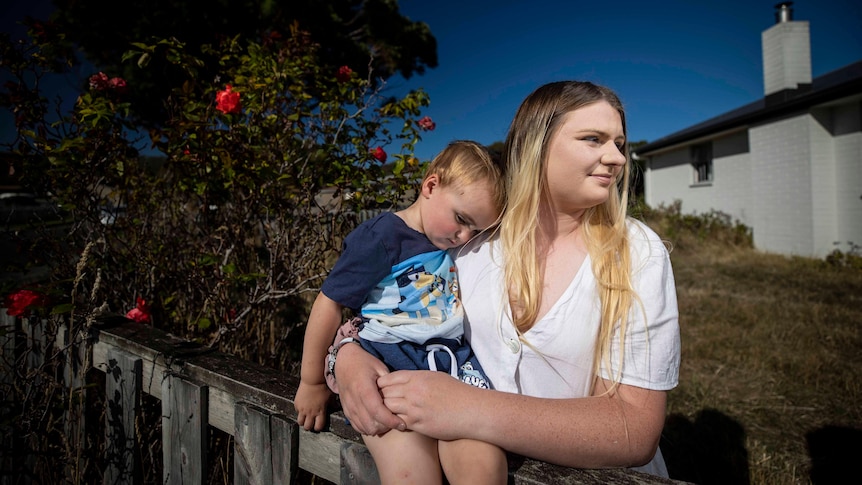  A young child rests on his mother who is looking off into the distance.