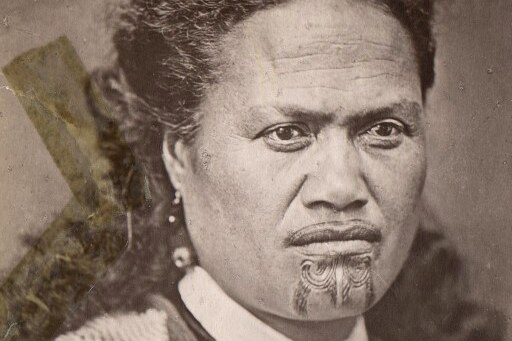 A sepia-toned archival image of a Maori woman with a tattooed chin and upper lip, and feathers in her hair.