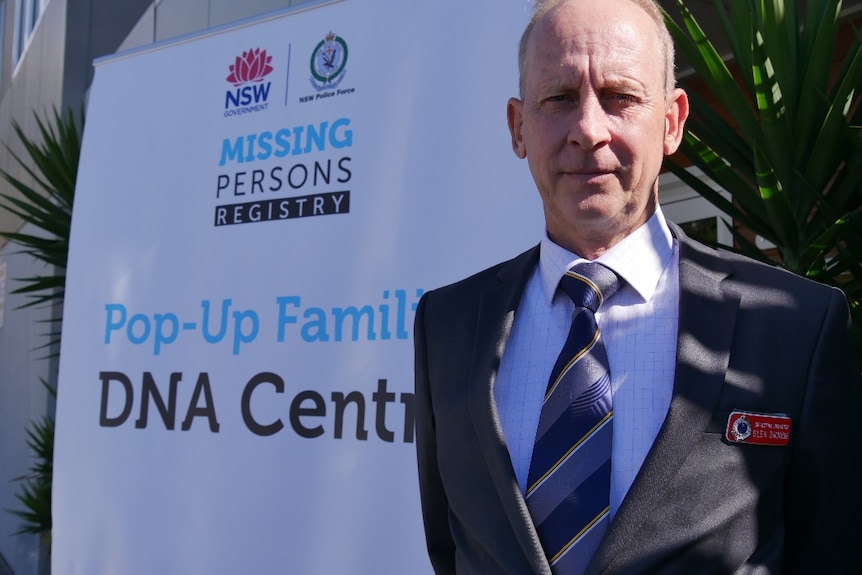 a man stands in a suit and tie in front of the 'pop up familial dna centre' sign