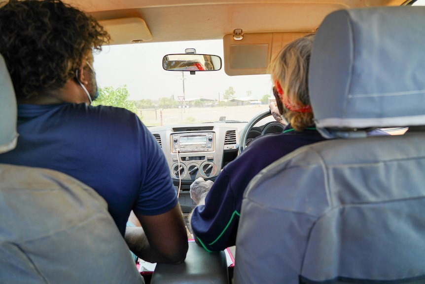 Two men sit in the cab of a ute, wearing masks.