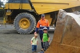 A man and two children stand beside heavy earthmoving machinery