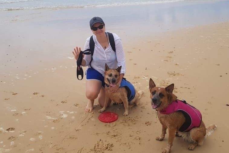 woman kneeling on beach with two dogs