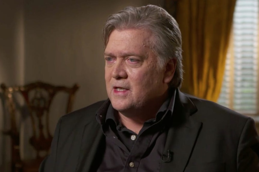 Steve Bannon sits in a chair wearing a coat and two shirts