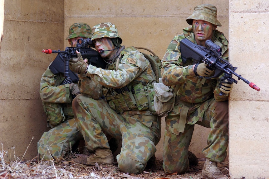 Army reservists with guns and wearing fatigues crouch down during an exercise.