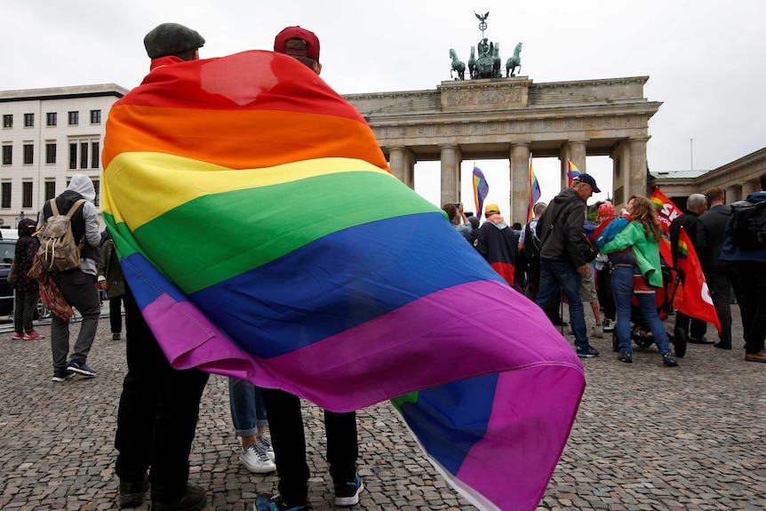 A couple wearing a same sex marriage flag celebrate in front of Berlin's Brandenburg gate.