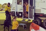 Dad and young children in caravan with kayak on green lawns.