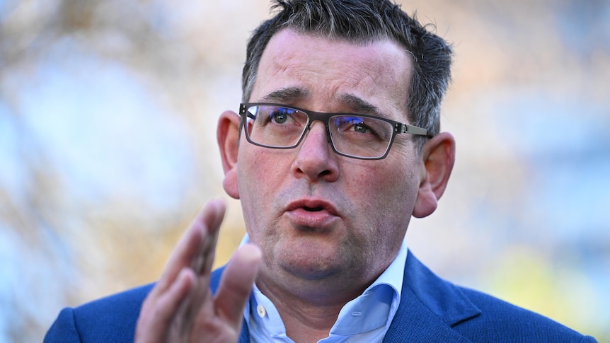 Daniel Andrews makes a hand gesture at a press conference. He is outdoors