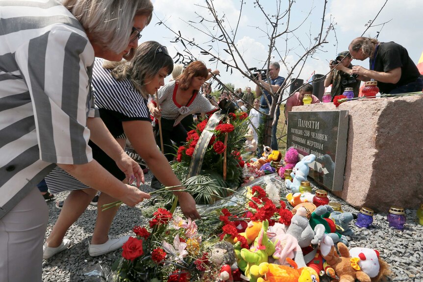 People place flowers and toys in front of a large stone with a Ukranian inscription commemorating the victims of flight MH17.
