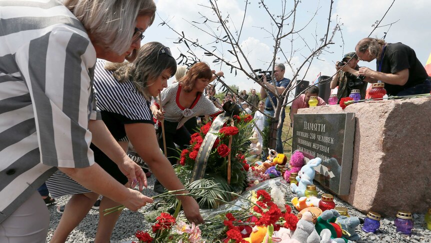 People place flowers and toys in front of a large stone with a Ukranian inscription commemorating the victims of flight MH17.