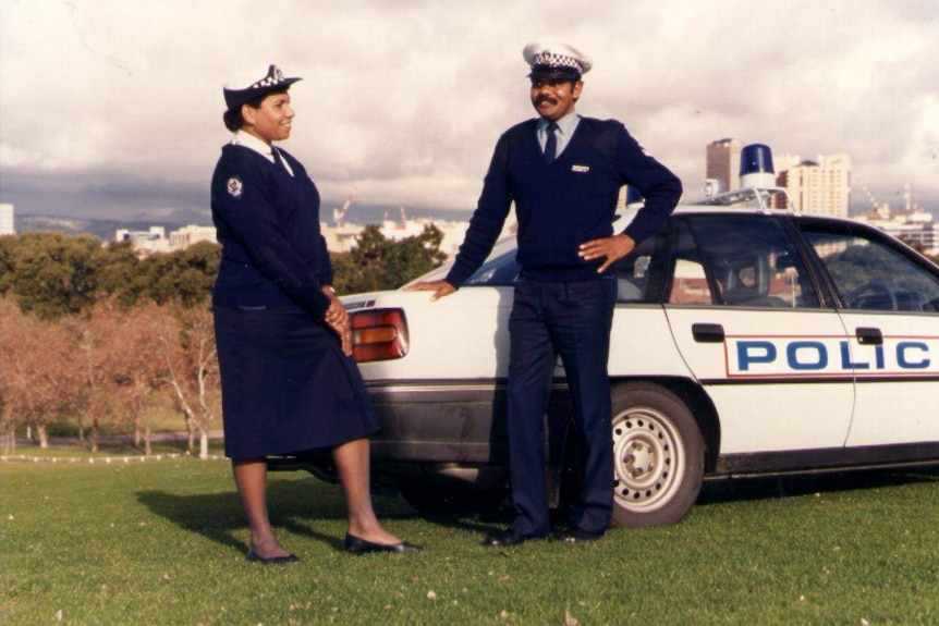 Leanne Liddle in police uniform stands next to a male police officer and white police car with the Adelaide city behind them.