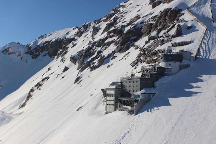 A rectangular main building with a round tower and other sections built onto the side of a snowy slope