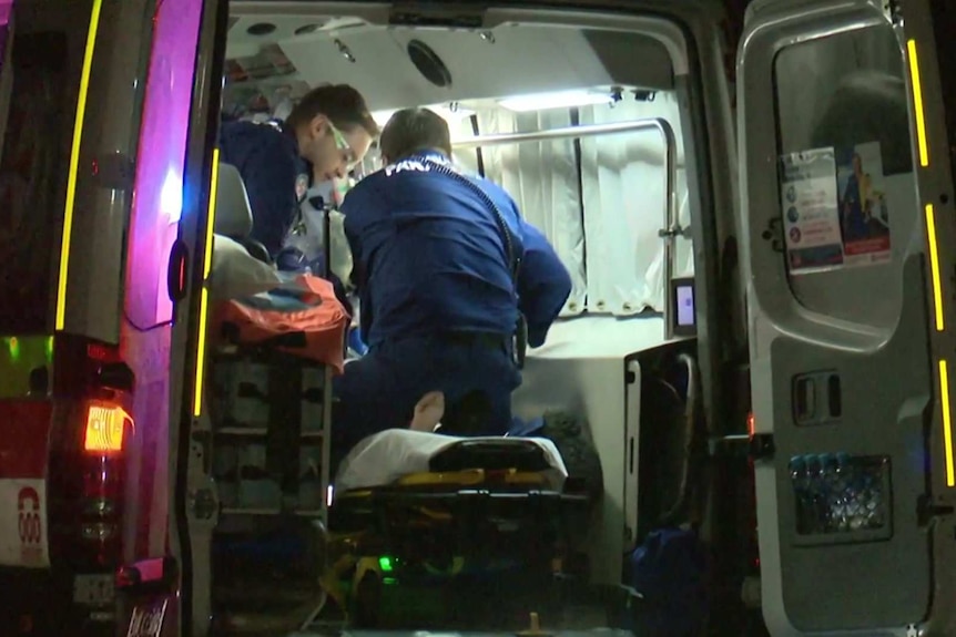 Paramedics treat an elderly man who lies on a stretcher in the back of an ambulance
